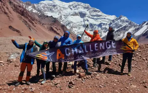 Grupa zdobywców z banerem "4 CHALLENGE" na tle ośnieżonego Aconcagui, najwyższego szczytu Andów.
