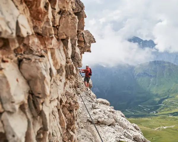 Wspinacz na via ferraty w Dolomitach, z widokiem na kręte drogi w dolinie.