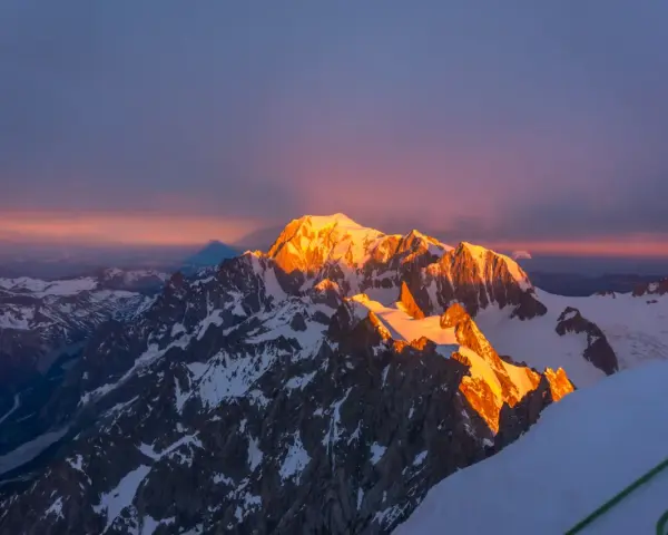 Mont Blanc latem, oświetlony złotym blaskiem wschodu słońca, z cieniem góry rzucającym się na niebo.