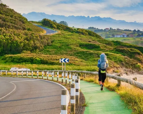 Pielgrzym z plecakiem idzie ścieżką wzdłuż wybrzeża, jedną z wielu tras Camino de Santiago.