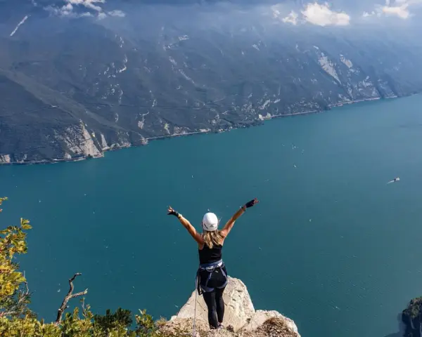 Kobieta w kasku i uprzęży cieszy się widokiem na jezioro Garda po pokonaniu via ferrata.