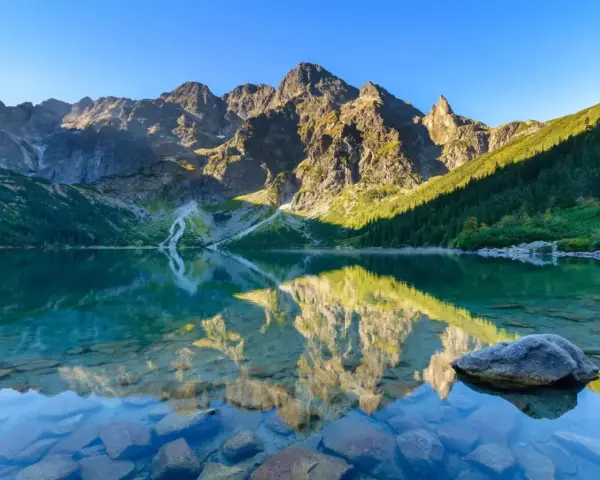 Idealny weekend w Tatrach: Morskie Oko odbija skaliste szczyty i zielone zbocza. Czysta woda odsłania kamienie.