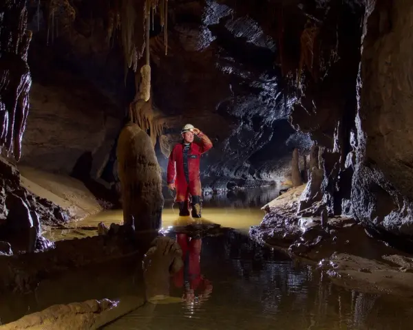 Eksplorator w jaskini, zanurzony po kolana w wodzie, odkrywa tajemnice speleologii. Stalagmity i nacieki tworzą niezwykły krajobraz.