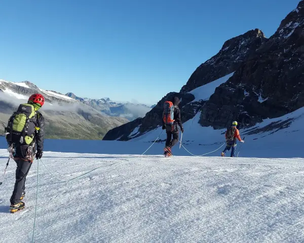 Trzej alpiniści na lodowcu, uczący się jak zostać przewodnikiem górskim. W tle majestatyczne szczyty.