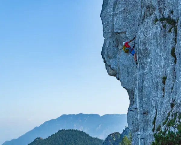Wspinacz pokonuje via ferrata niemcy, zmagając się z pionową ścianą skalną. W tle piękne góry.