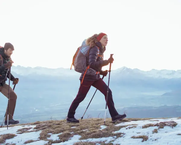 Para, co to jest hiking? To dwójka ludzi z plecakami i kijkami, idących po ośnieżonym szlaku w górach.