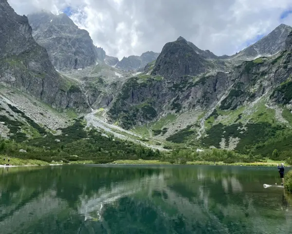 Piękne szlaki na Słowacji. Jezioro w górach odbija skaliste szczyty i zielone zbocza.