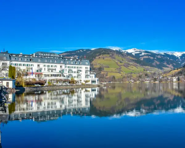 Grand Hotel nad jeziorem w Zell am See, z odbiciem w spokojnej wodzie i ośnieżonymi górami w tle.