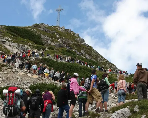 Tłum turystów podąża czerwonym szlakiem na Giewont. W oddali widoczny krzyż.