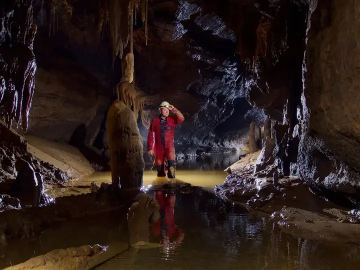 Eksplorator w jaskini, zanurzony po kolana w wodzie, odkrywa tajemnice speleologii. Stalagmity i nacieki tworzą niezwykły krajobraz.