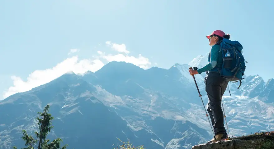Kobieta z plecakiem i kijkami trekkingowymi podziwia majestatyczne góry w drodze na mount everest base camp.