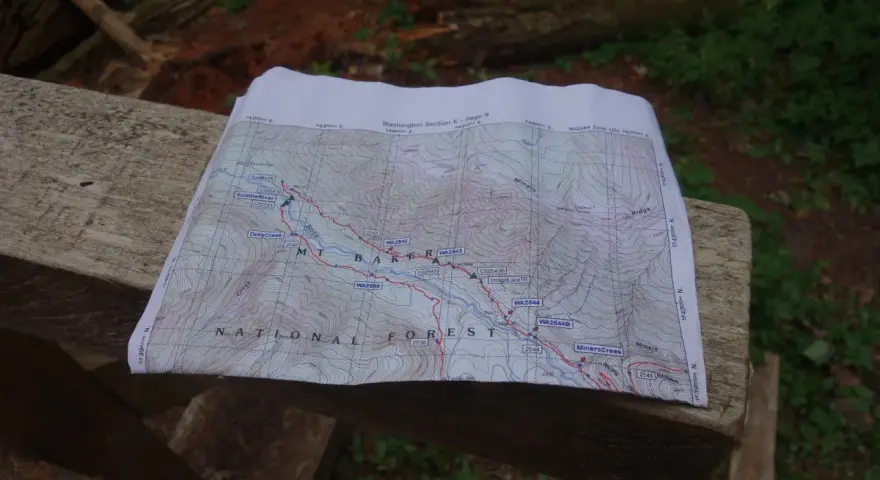 Mapa szlaku grzbietu pacyficznego z zaznaczonymi punktami i rzekami, leżąca na drewnianej ławce.