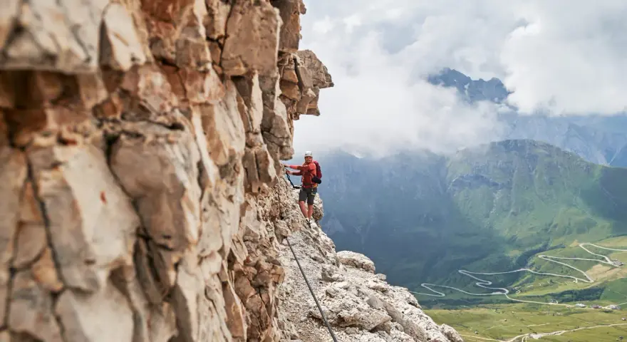 Wspinacz na via ferraty w Dolomitach, z widokiem na kręte drogi w dolinie.
