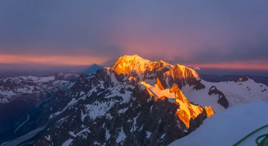 Mont Blanc latem, oświetlony złotym blaskiem wschodu słońca, z cieniem góry rzucającym się na niebo.