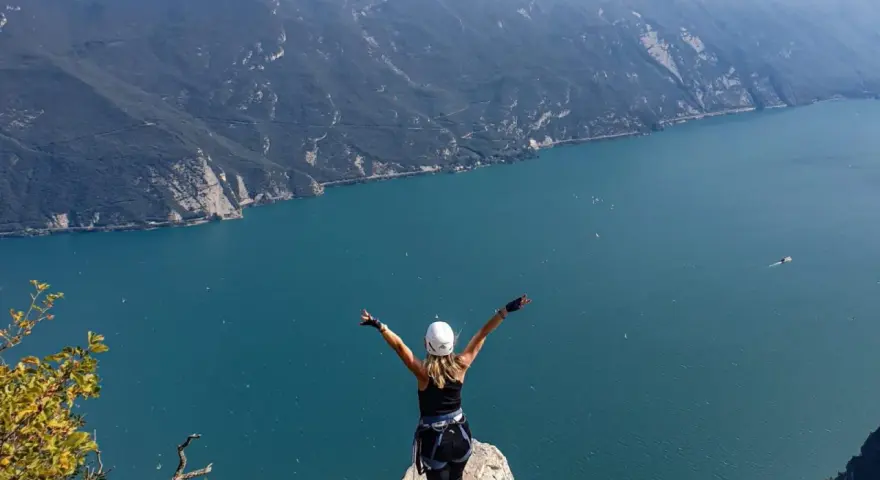 Kobieta w kasku i uprzęży cieszy się widokiem na jezioro Garda po pokonaniu via ferrata.
