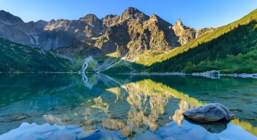 Idealny weekend w Tatrach: Morskie Oko odbija skaliste szczyty i zielone zbocza. Czysta woda odsłania kamienie.