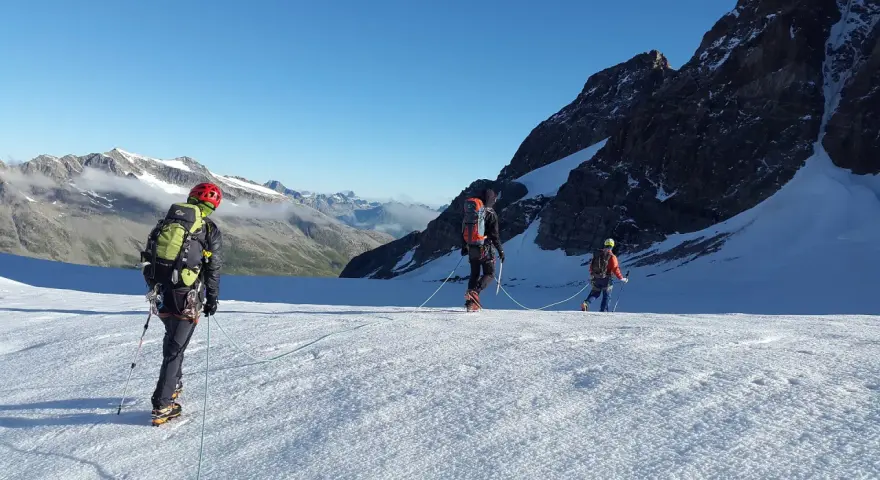 Trzej alpiniści na lodowcu, uczący się jak zostać przewodnikiem górskim. W tle majestatyczne szczyty.