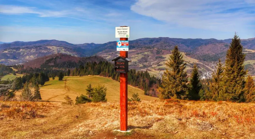 Wysoki Wierch w Pieninach, szlak turystyczny z tabliczką i skrzynką na pieczątki. W tle malownicze wzgórza i lasy.