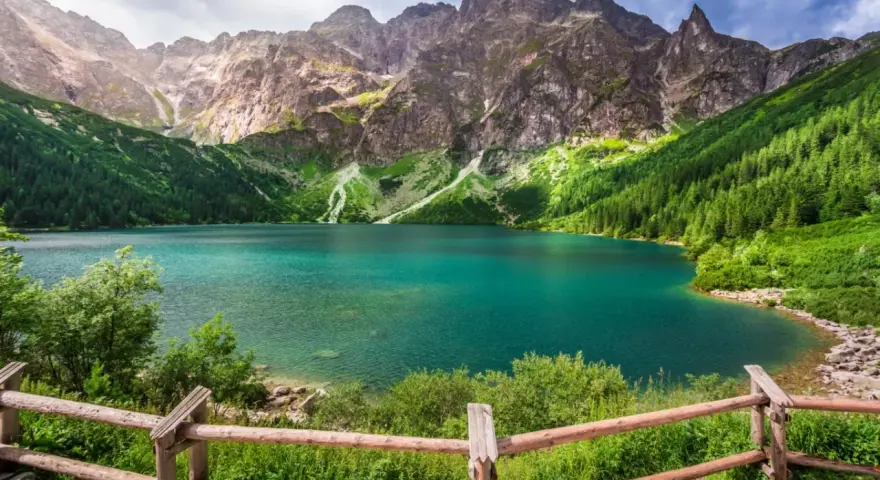 Turkusowe jezioro otoczone zielonymi zboczami gór i lasem, przypominające beskidzkie Morskie Oko.