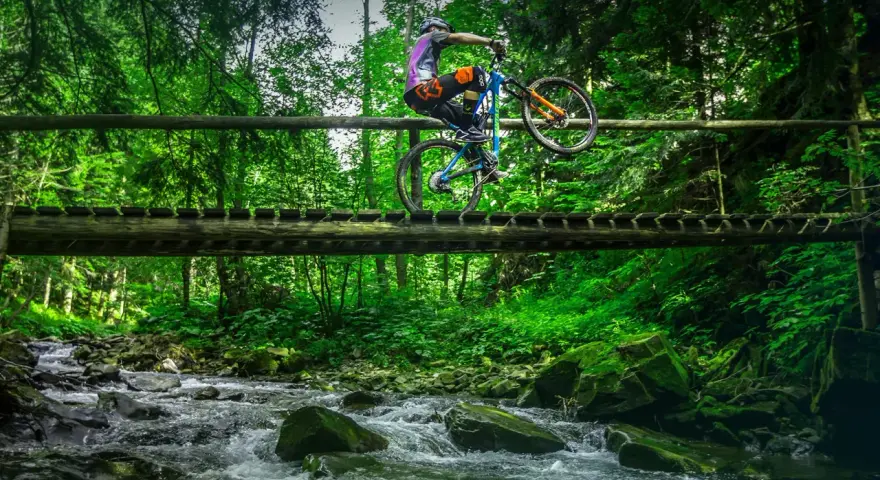 Rowerzysta wykonuje trik na drewnianym moście nad potokiem. Wspaniałe trasy rowerowe Zakopane czekają na odkrycie!