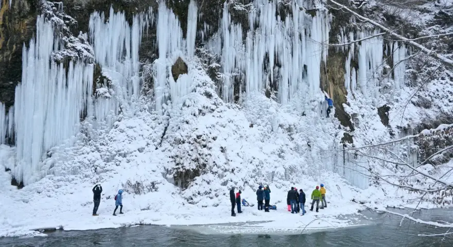 Lodowe wodospady w Rudawce Rymanowskiej zimową porą. Grupa ludzi obserwuje wspinaczkę lodową. Jak dojechać?