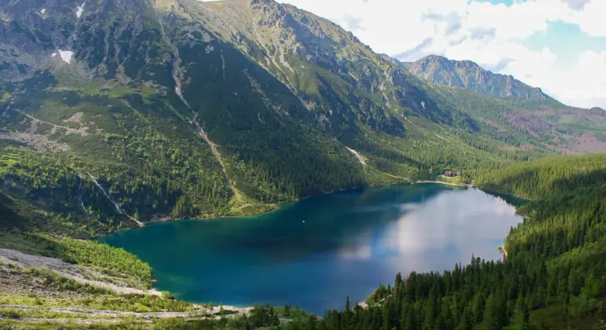 Największe jezioro w Tatrach, Morskie Oko, otoczone zielonymi lasami i skalistymi szczytami.