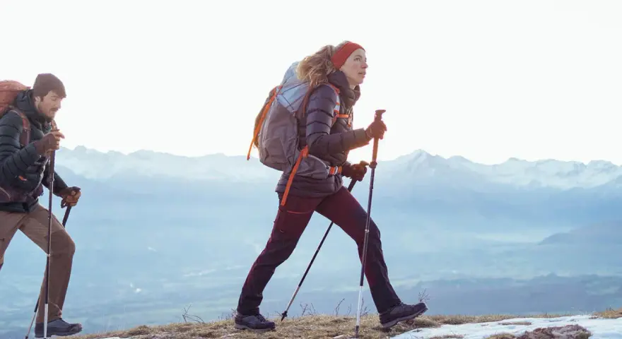 Para, co to jest hiking? To dwójka ludzi z plecakami i kijkami, idących po ośnieżonym szlaku w górach.