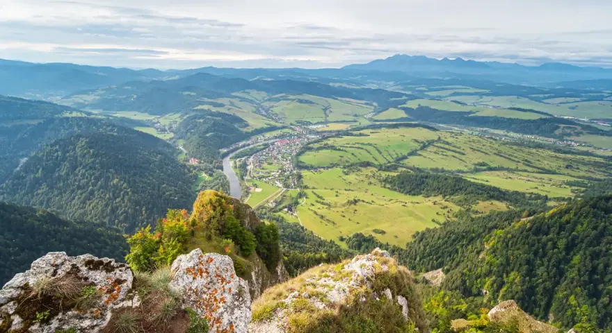 Widok z góry na dolinę z rzeką i miasteczkiem, w oddali majaczą Tatry. Widok przypomina trzy korony.