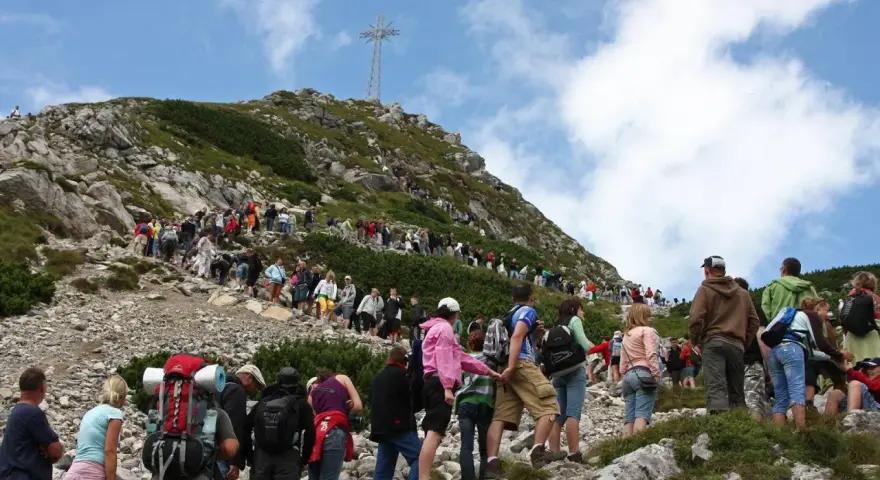 Tłum turystów podąża czerwonym szlakiem na Giewont. W oddali widoczny krzyż.
