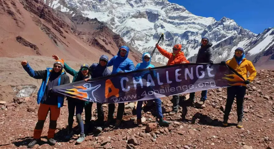 Grupa zdobywców z banerem "4 CHALLENGE" na tle ośnieżonego Aconcagui, najwyższego szczytu Andów.