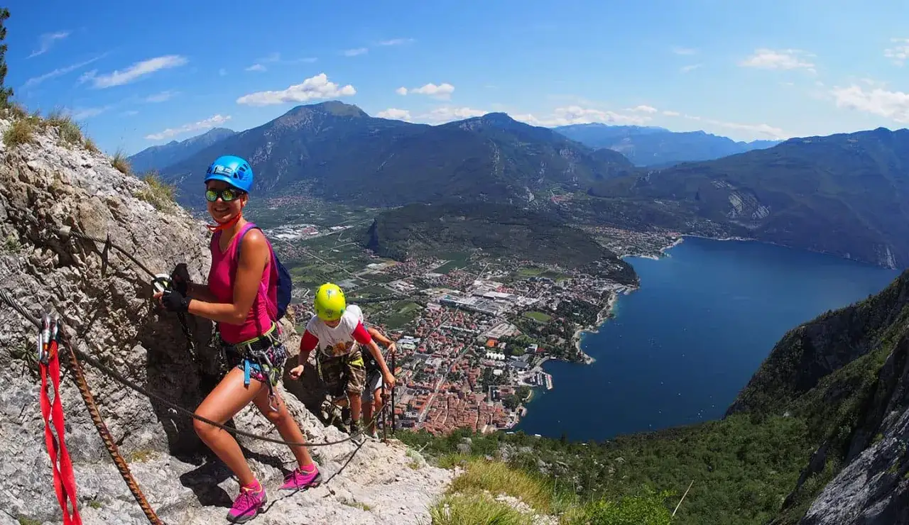 Rodzina pokonuje via ferrata Garda, podziwiając malowniczy widok na jezioro i miasteczko.