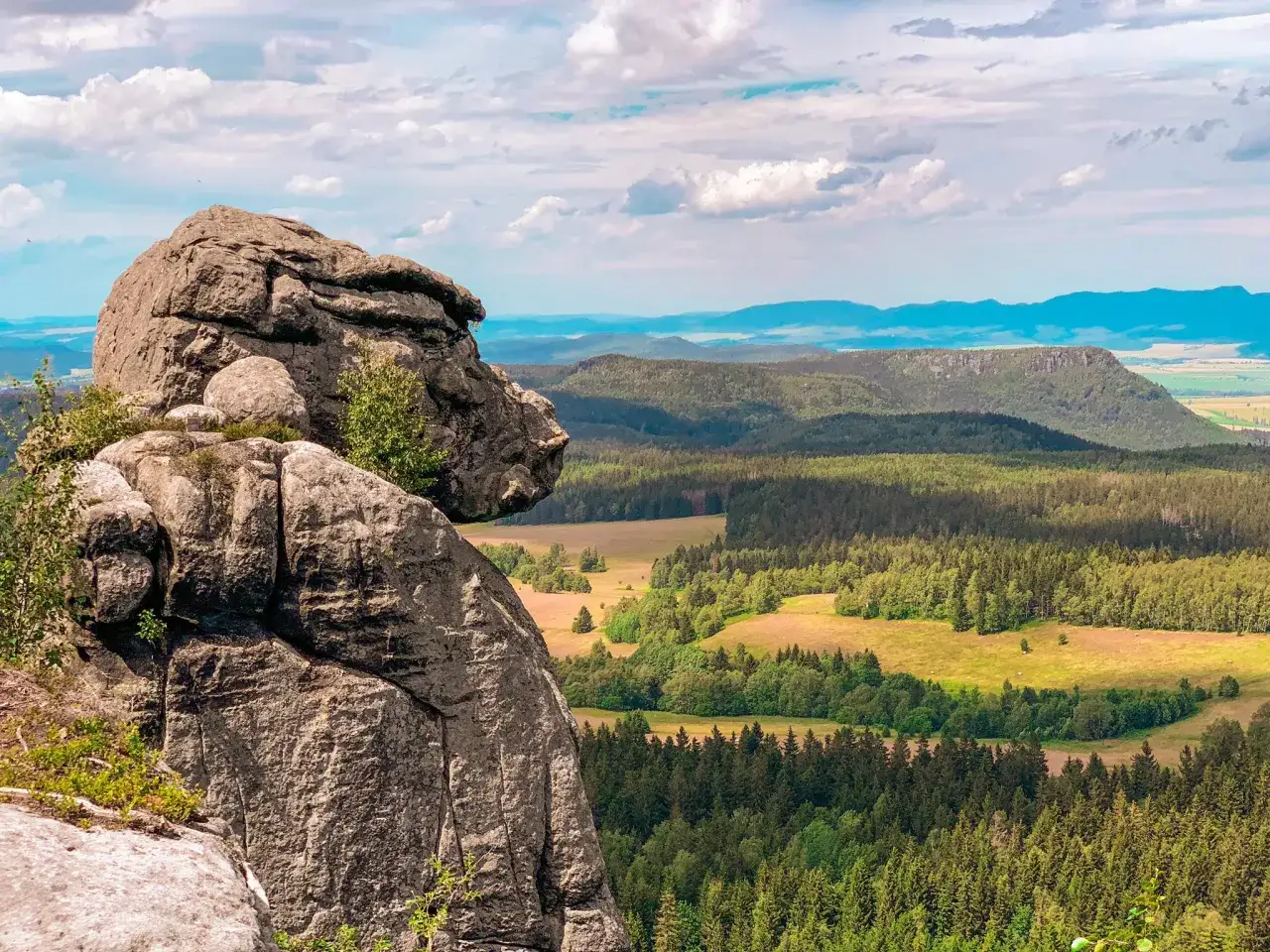 Skaliste formacje Gór Stołowych górują nad zielonymi lasami i polami. Widok zapiera dech w piersiach.