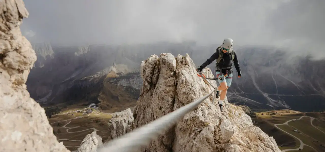 Kobieta w kasku i sprzęcie wspinaczkowym pokonuje via ferrata niemcy, balansując na linie nad przepaścią.