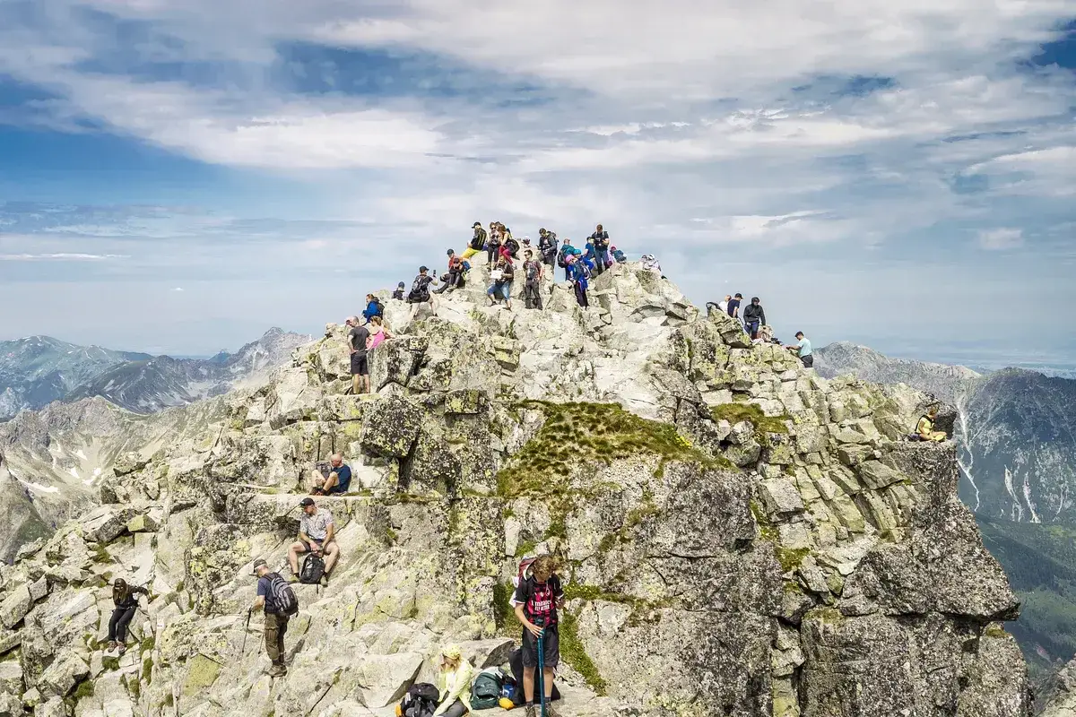 Grupa turystów na skalistym szczycie Rysów. Widok na Tatry, chmury na niebie. Ile się idzie na Rysy? To zależy od kondycji!