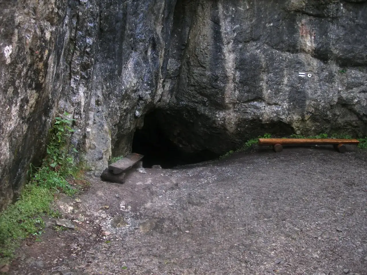 Wejście do jednej z jaskiń w Zakopanem. Obok ciemnego otworu skalnego stoją drewniane ławki, zachęcające do odpoczynku.