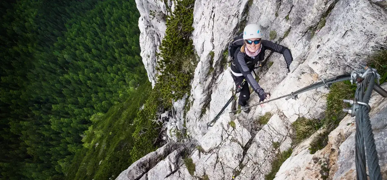 Kobieta wspina się po via ferracie w Dolomitach, podziwiając rozległy las.