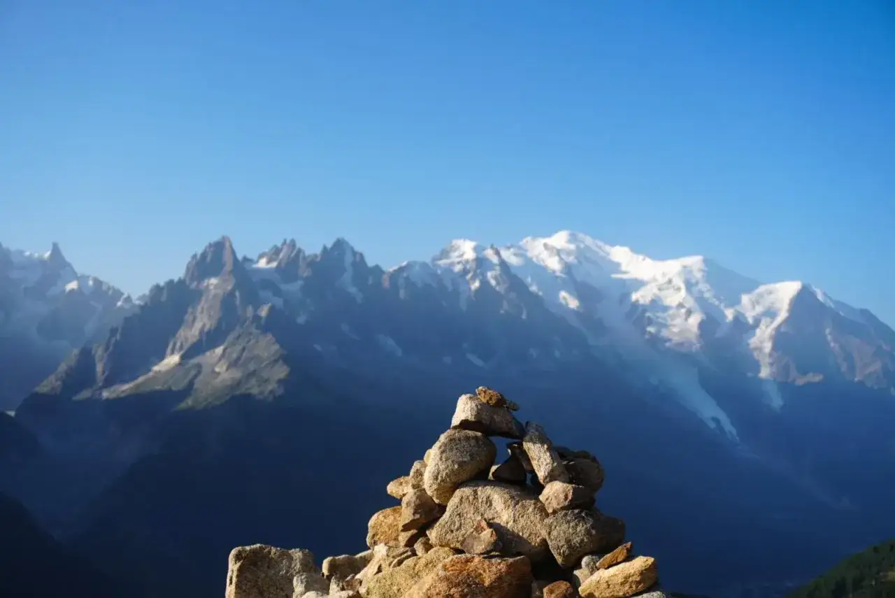 Kamienny kopczyk na szlaku Tour du Mont Blanc, z majestatycznym, ośnieżonym masywem w tle.