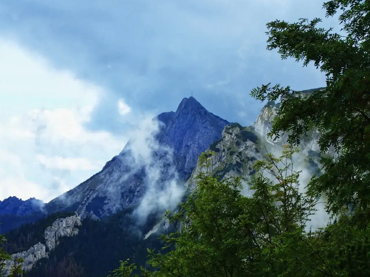 Mglisty Giewont, z krzyżem na szczycie, widziany z zielonego lasu. Czerwony szlak na Giewont wzywa do wspinaczki.