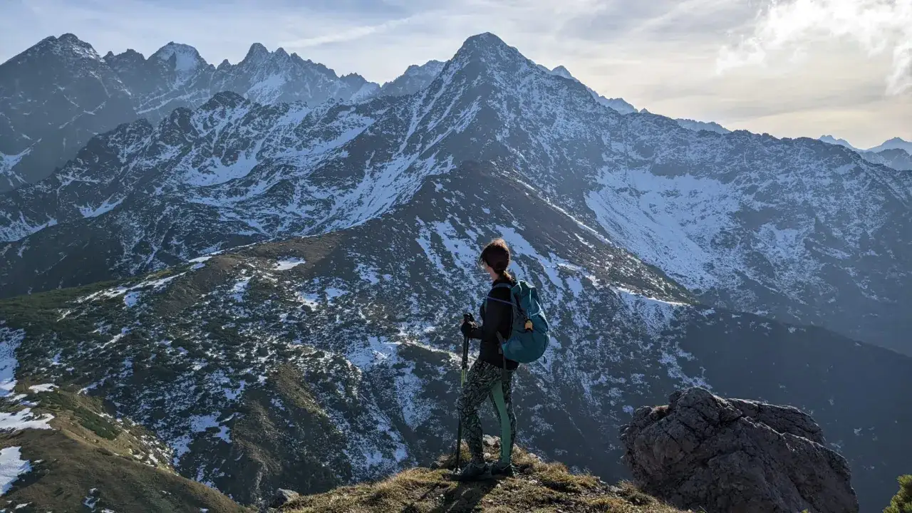 Osoba z plecakiem i kijkami podziwia ośnieżone szczyty Tatr Bielskich. Wspaniałe tatry bielskie szlaki czekają na odkrycie.