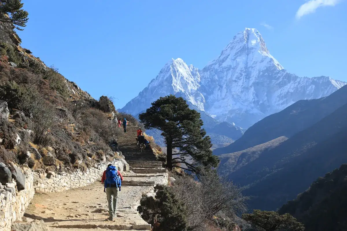 Trekking do Everest Base Camp, gdzie koszty są wysokie, ale widoki zapierają dech w piersiach. Grupa turystów wspina się po kamiennych schodach w kierunku ośnieżonych szczytów.