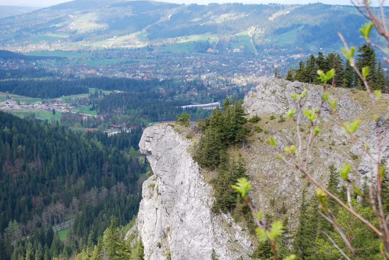 Widok na dolinę z górami i lasami. Na pierwszym planie skalista ściana, przypominająca zapora pod nosem.