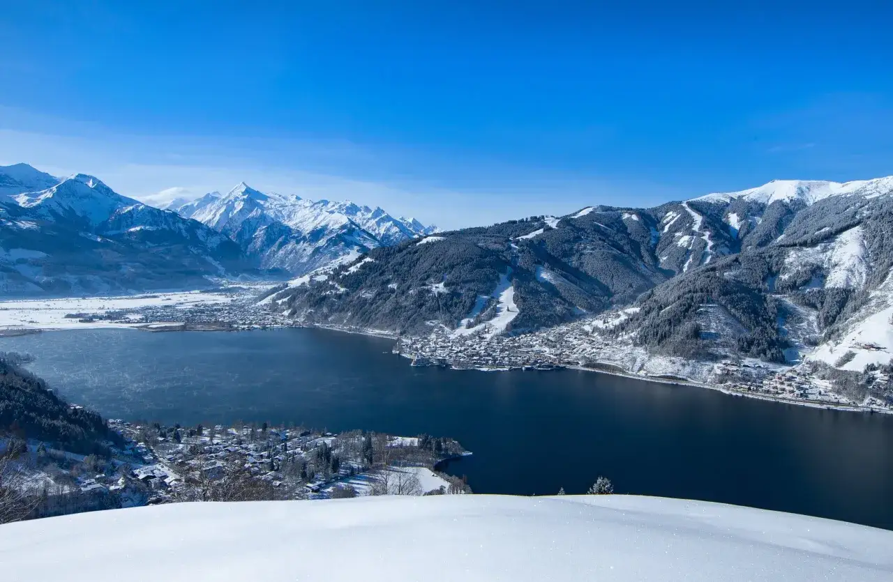 Zell am See zimową porą: ośnieżone g&oacute;ry, ciemny, spokojny akwen i urokliwe miasteczko w dole.