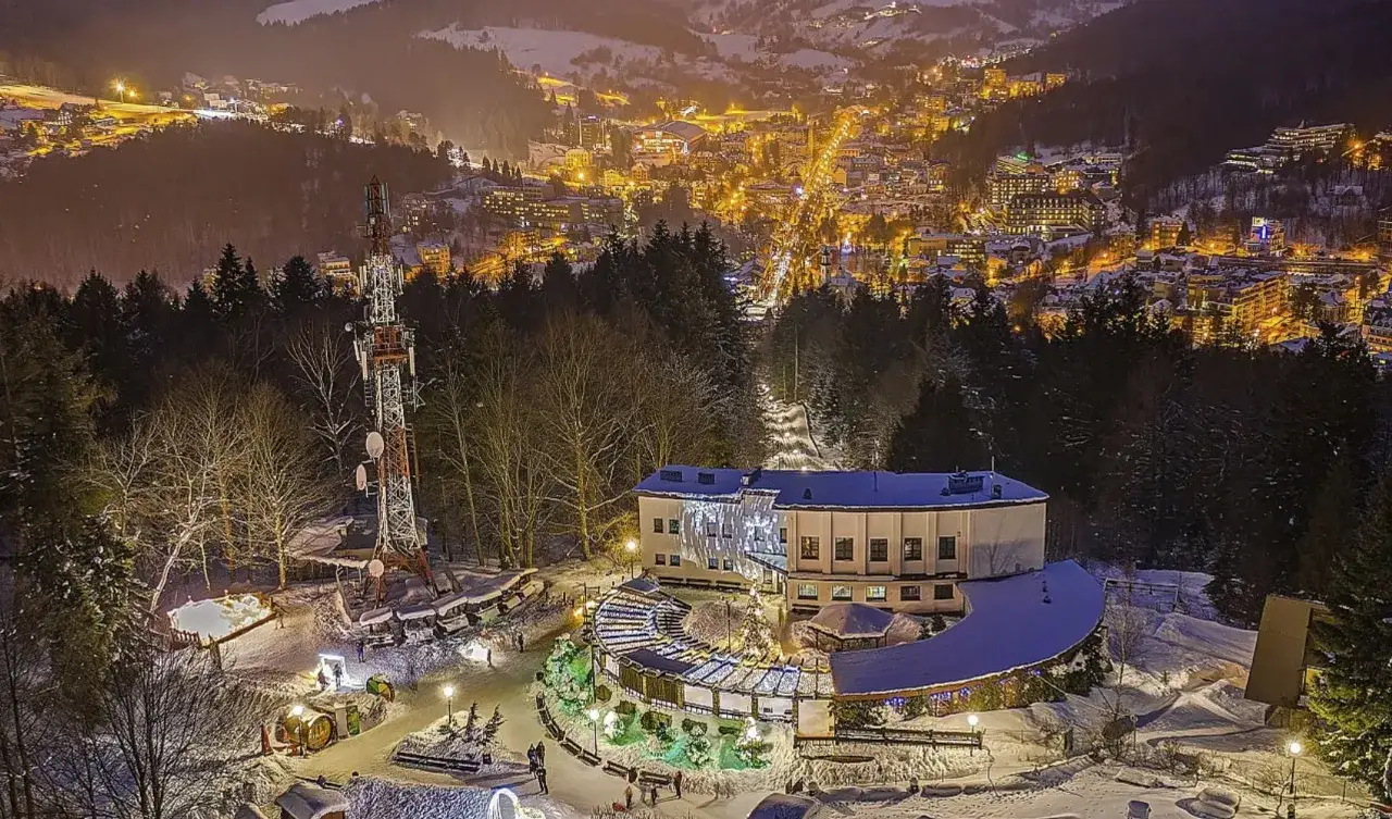 G&oacute;ra Parkowa w Krynicy nocą. Widok na oświetlone miasto, wieżę telekomunikacyjną i budynek z iluminacjami. Wejście do parku zimową porą.
