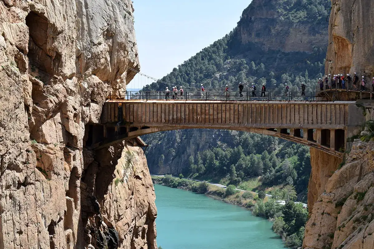 Spacerzy po Caminito del Rey, wąska ścieżka wzdłuż skalnych ścian nad turkusową rzeką.