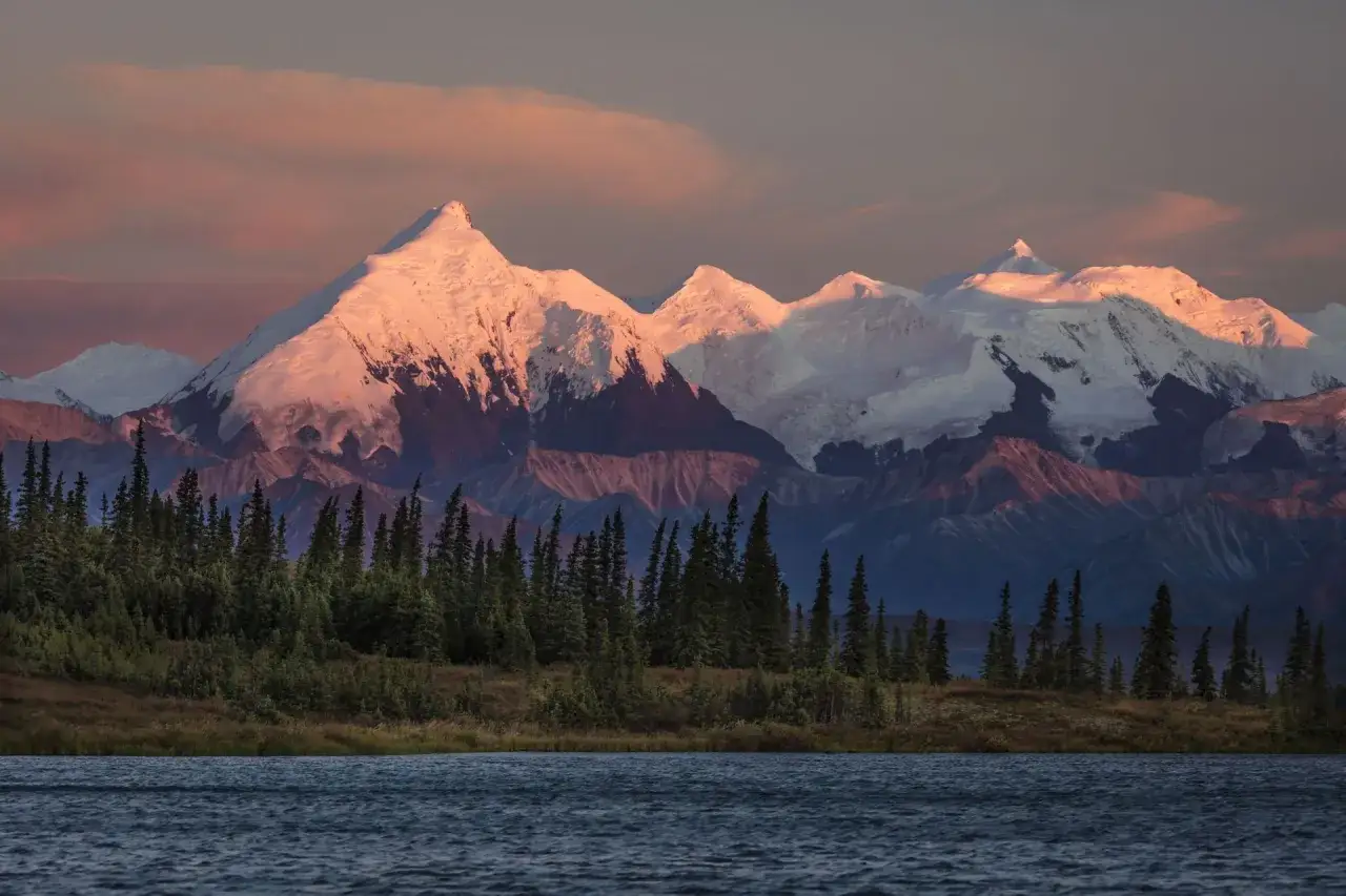 Zachód słońca oświetla najwyższy szczyt Ameryki, Denali, nad jeziorem i lasem.