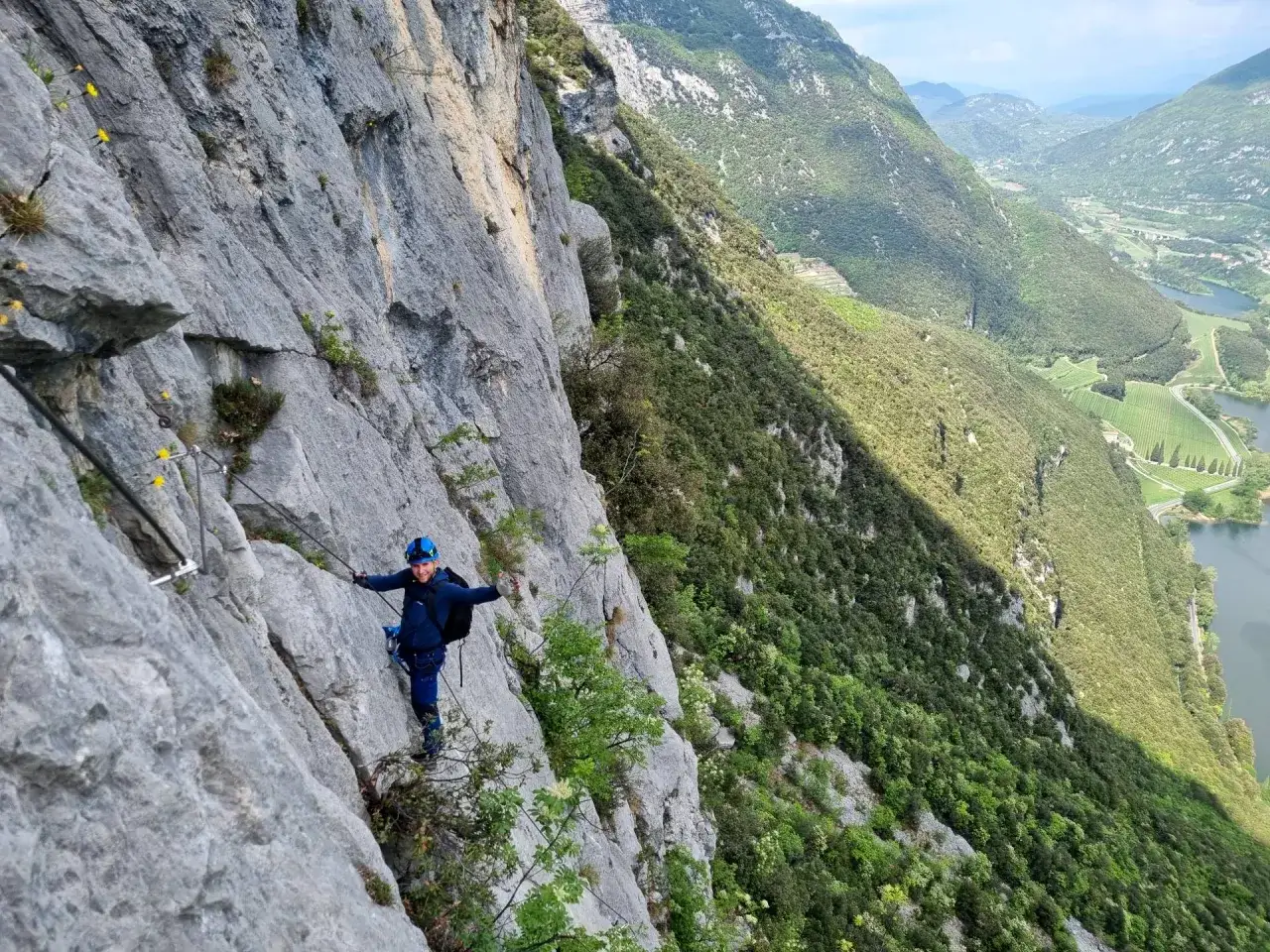 Uśmiechnięty turysta na via ferrata Garda, z widokiem na jezioro i zielone doliny.