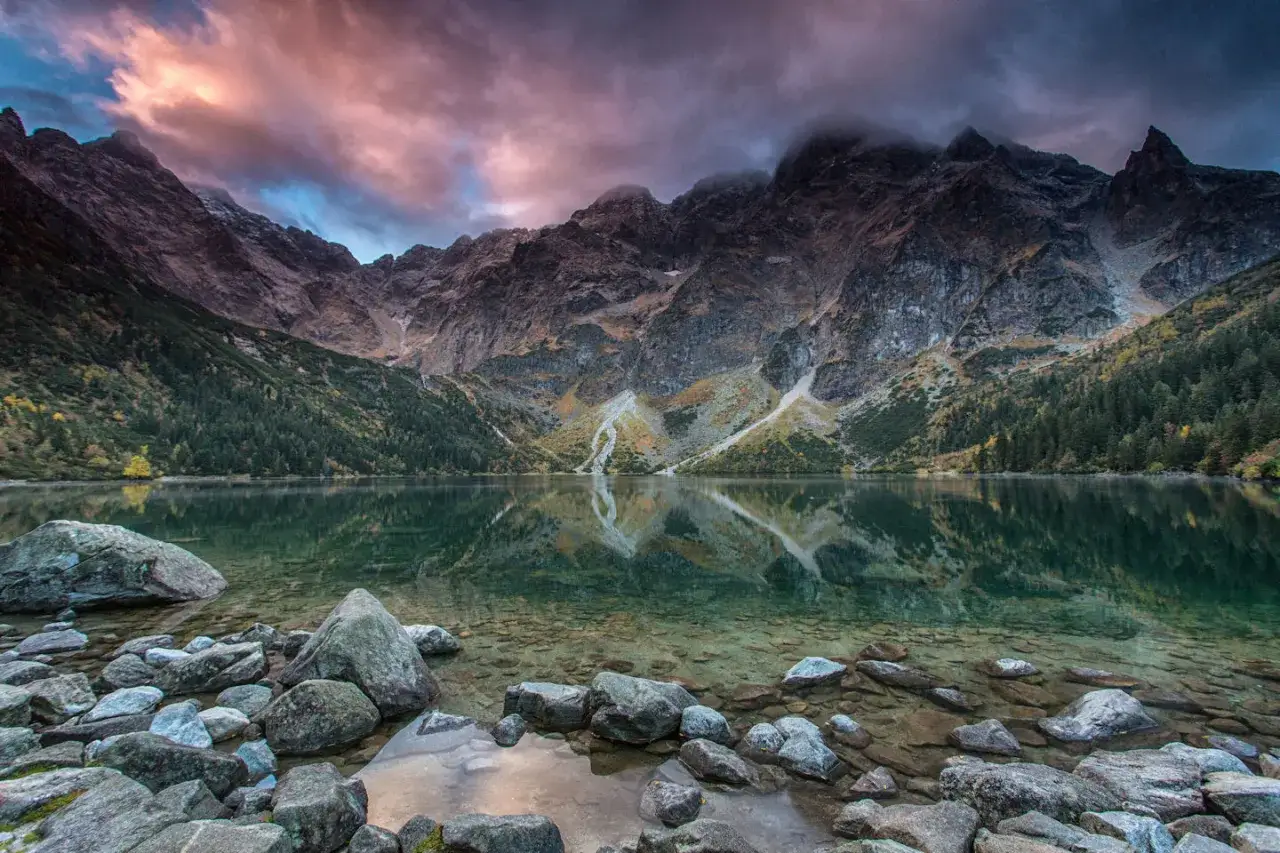 Morskie Oko latem, z kamienistym brzegiem i odbijającymi się w tafli wody skalistymi szczytami Tatr.