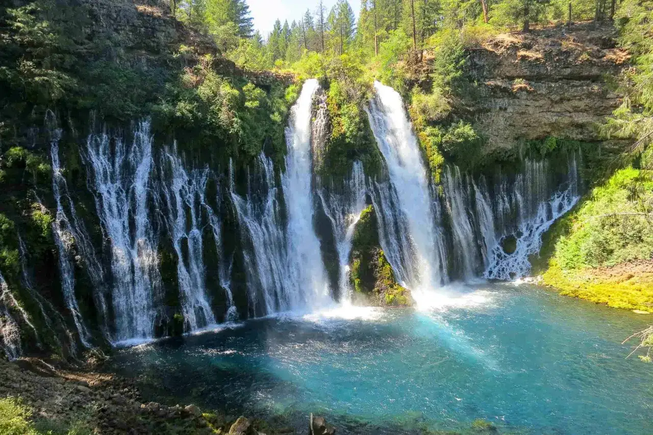 Wodospady Burney Falls, część szlaku grzbietu pacyficznego, kaskadami spływają po skalnej ścianie do turkusowej wody.