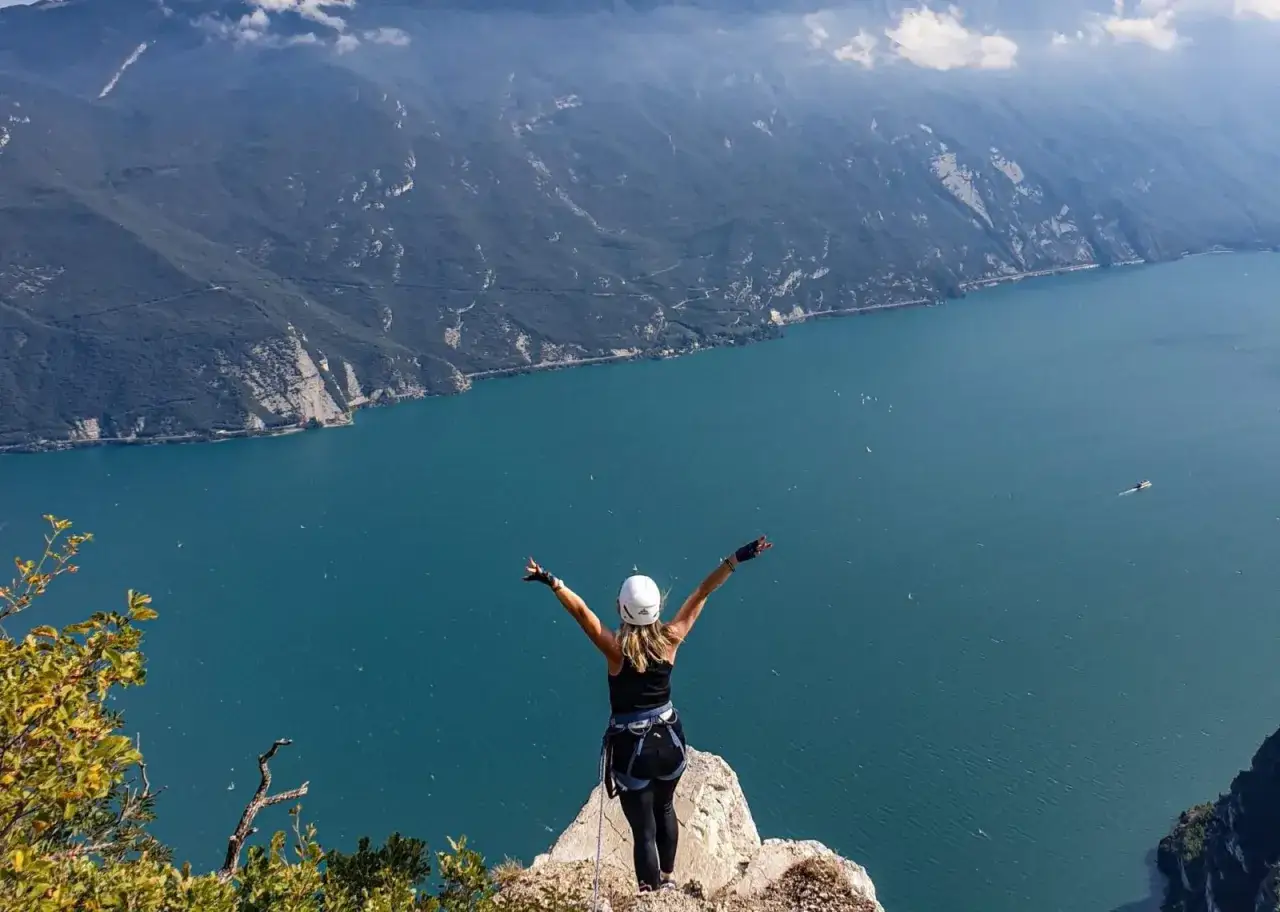 Kobieta w kasku i uprzęży cieszy się widokiem na jezioro Garda po pokonaniu via ferrata.