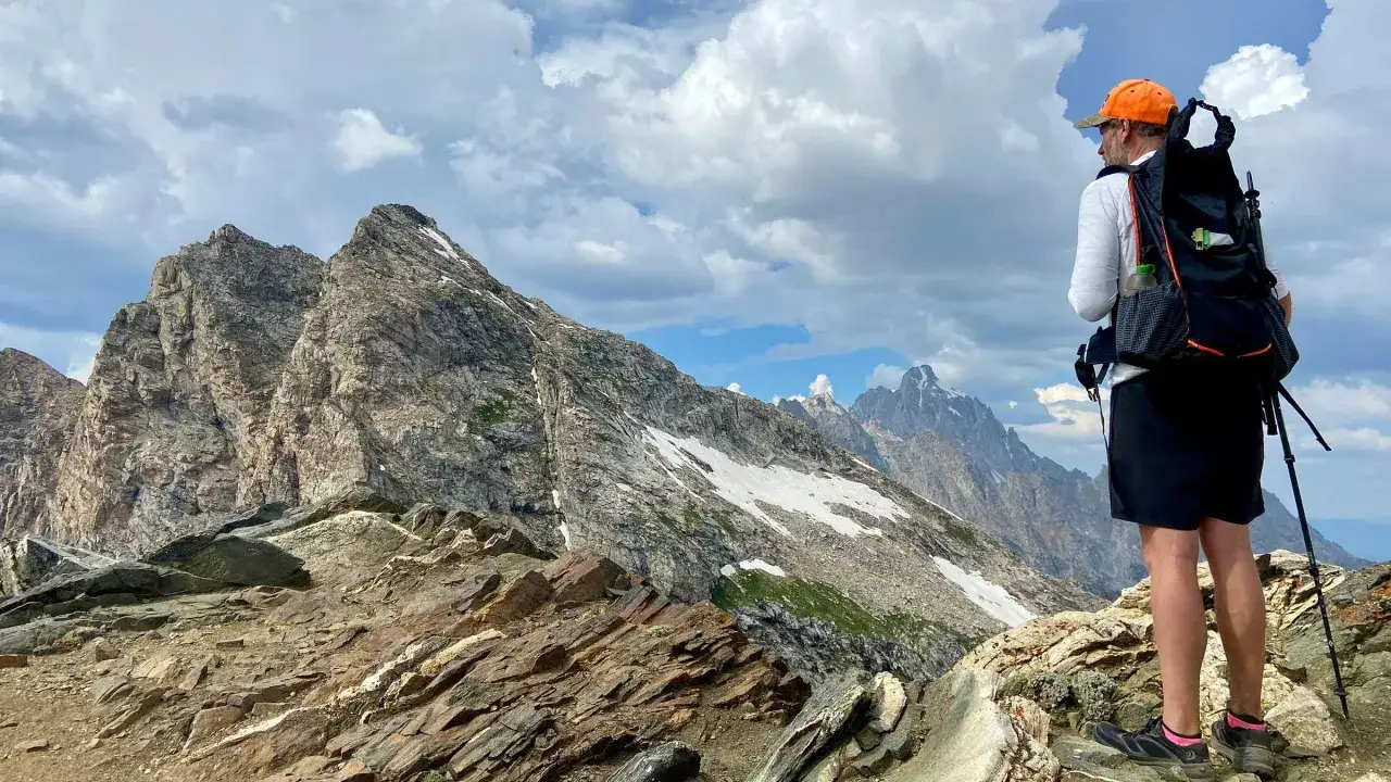 Osoba z plecakiem i kijami trekkingowymi podziwia majestatyczne góry. To właśnie jest hiking – przygoda na szlaku!